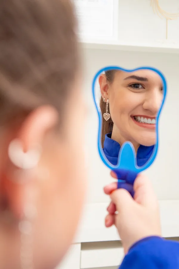 Dra. Lara Gimenez de uniforme azul, com o rosto refletido em um espelho em formato de dente